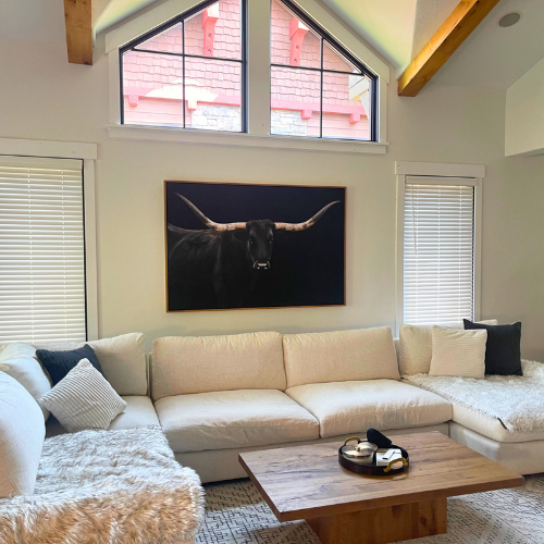Window coverings in living room, white couch, bull painting, pillows & blankets